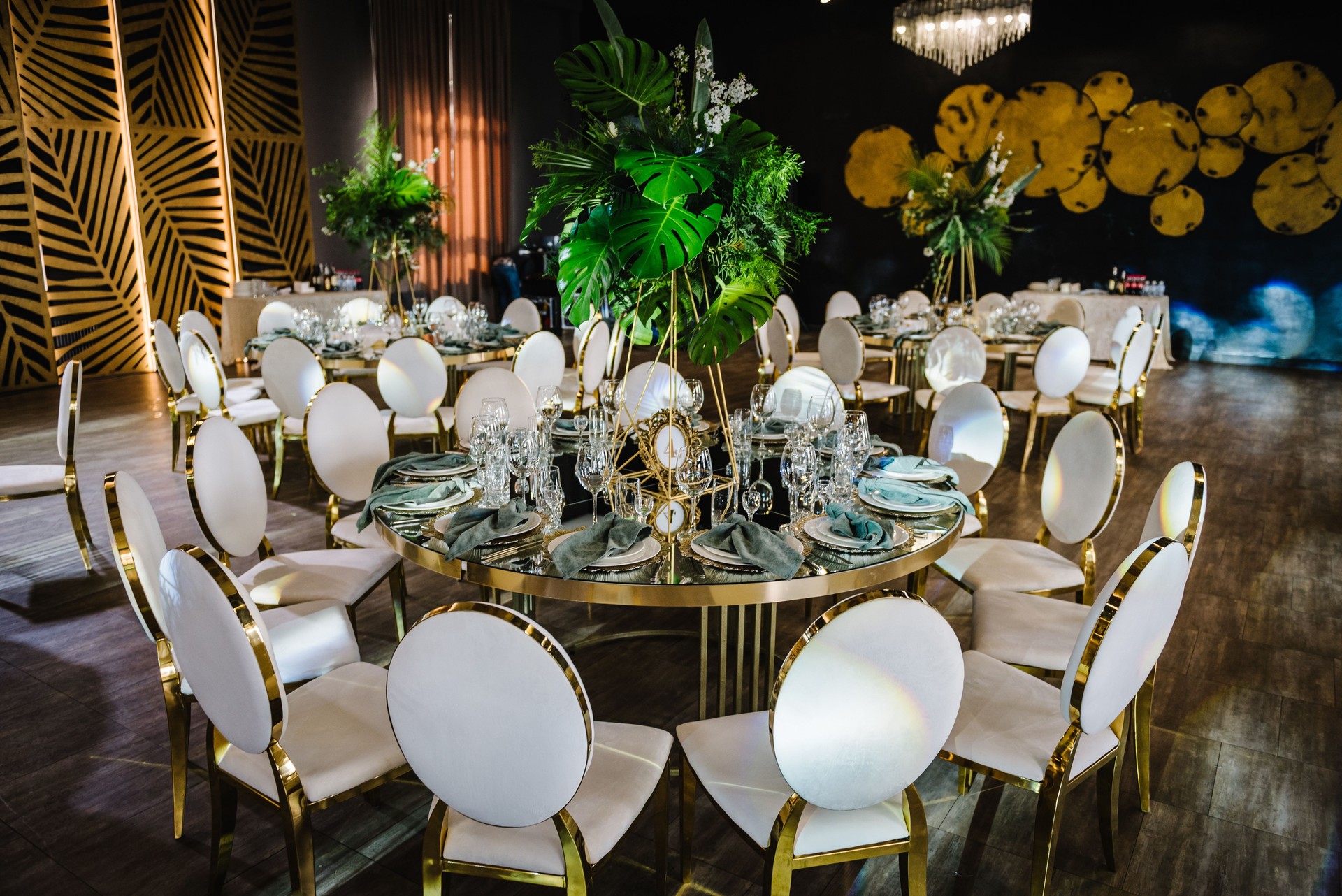 Round served banquet tables ready for guests, decorated table with plate, glasses, forks, emerald green napkins. Elegant dinner table. Beautifully organized event. Wedding hall with atmospheric decor.
